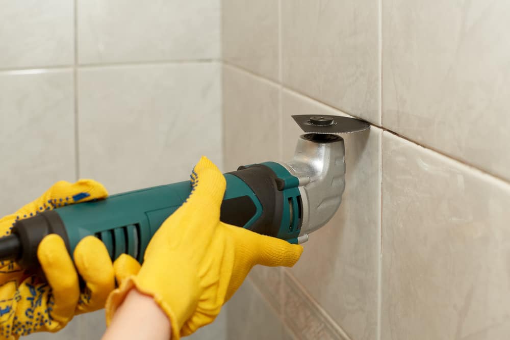 Male hands with renovator multi-tool removing the old grout