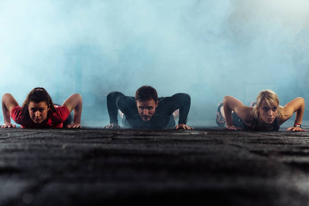 Attractive athletic young people doing press-ups in a gym surrounded by smoke