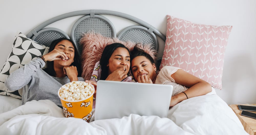 Girls having a sleepover enjoying a movie on laptop with popcorns