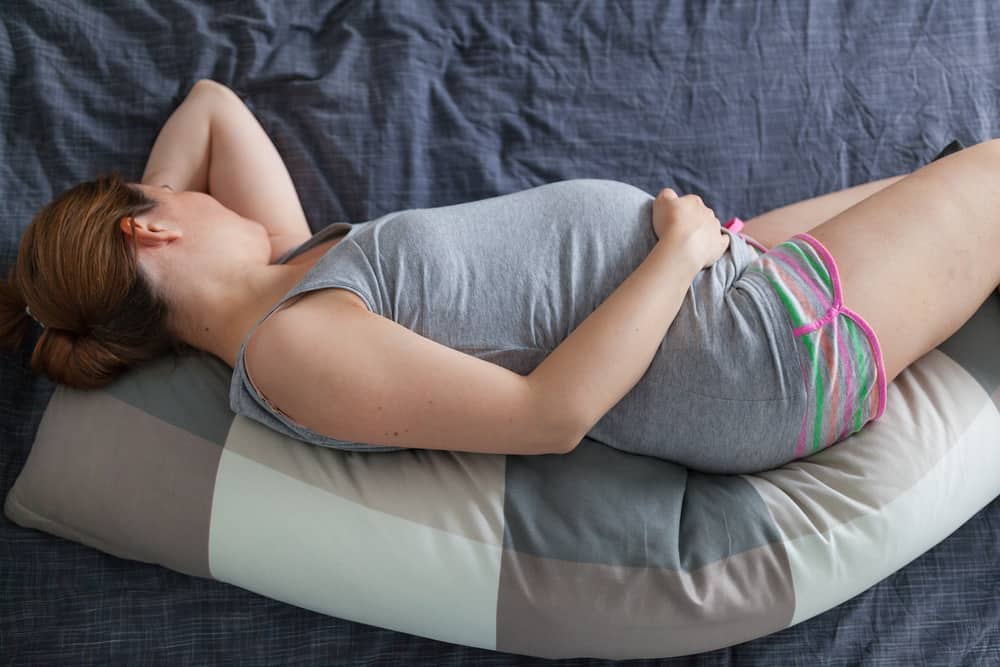 Young pregnant woman lying in bed with pregnancy pillow.